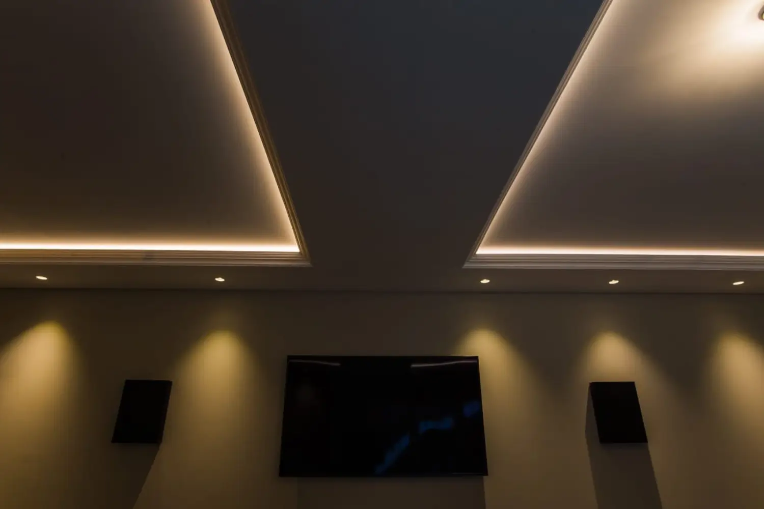 Modern ceiling with recessed LED lighting, downlights, and a wall-mounted television with surround sound speakers, designed by Rajvar Technologies.