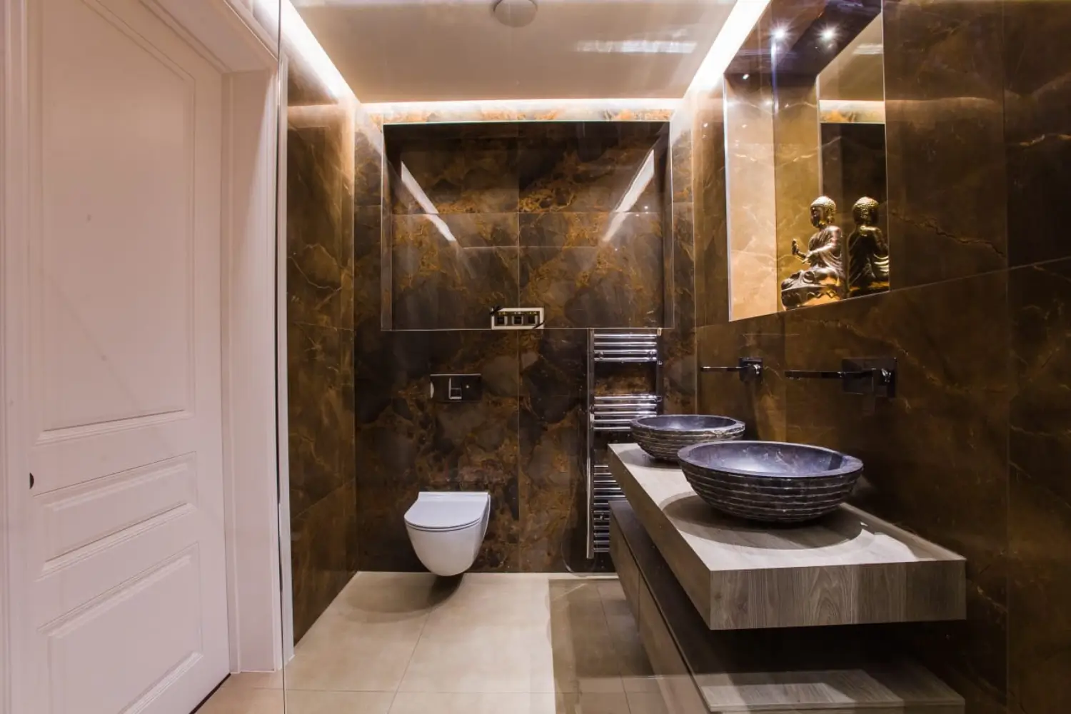 Luxurious bathroom with dark marble walls, modern floating vanity with twin vessel sinks, wall-mounted taps, heated towel rail, and decorative Buddha statues, designed by Rajvar Technologies.