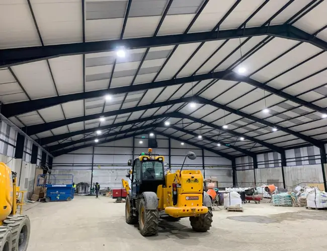 Interior of a large warehouse built by Rajvar, featuring a yellow construction vehicle and building materials under bright overhead lighting.