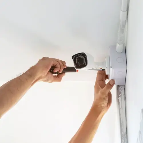 Technician installing a CCTV security camera on a white ceiling – Rajvar Technologies.